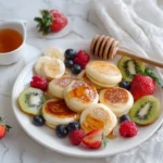 Fluffy mini pancakes served with fresh fruits and syrup.