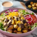 Assembling a burger bowl with potatoes, toppings, cheese, and sauce